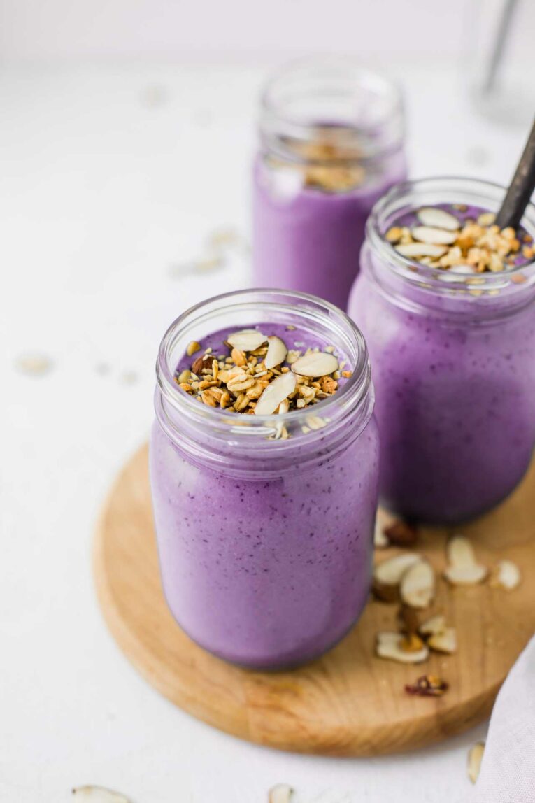 Creamy, sweet, tasty, and one of the BEST protein shakes out there! This Blueberry Vanilla Protein Shake Recipe is made with fresh or frozen blueberries, creamy greek yogurt, your choice of milk, and vanilla protein powder. Make this easy snack or breakfast in 5 minutes or less! Easy to make blueberry vanilla protein shakes on a cutting board.