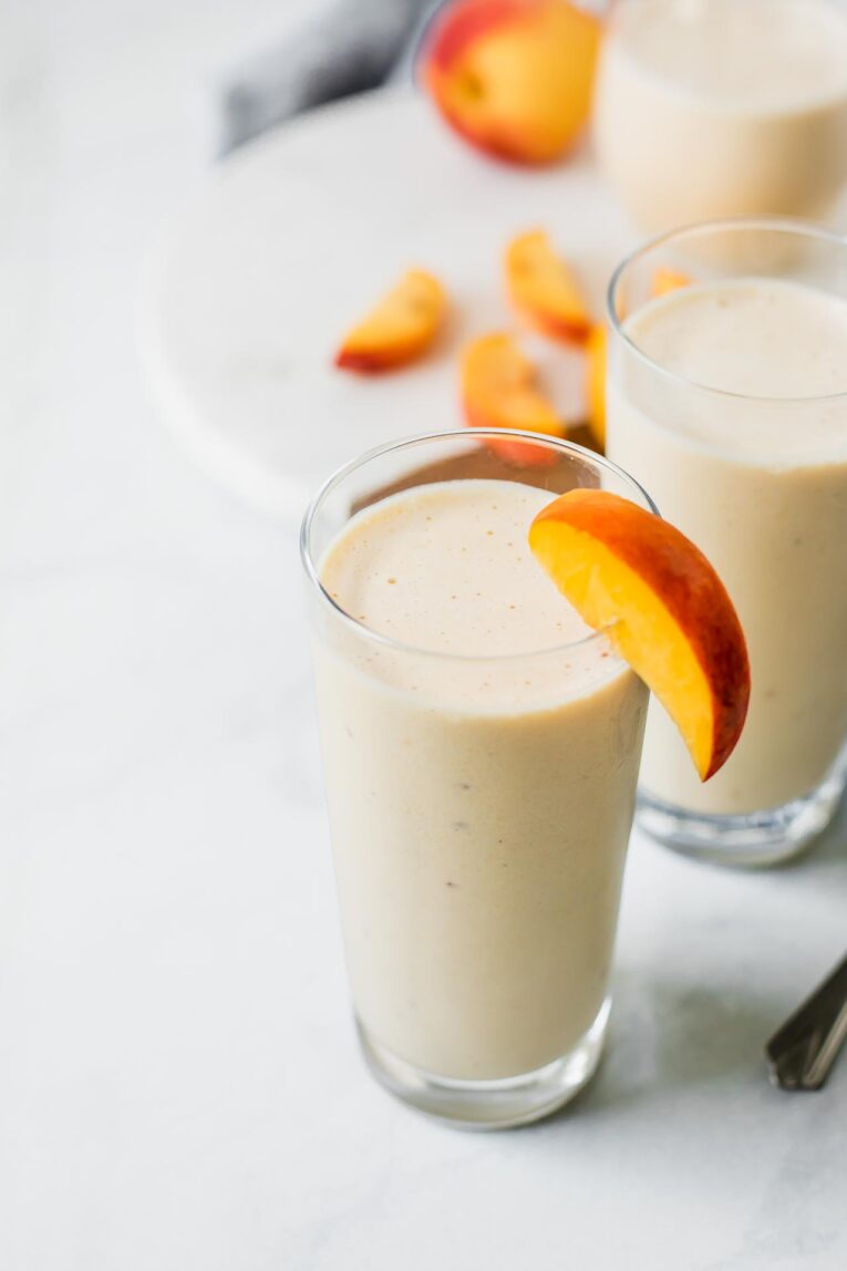 Angled shot of a peach yogurt smoothie with peach slices.