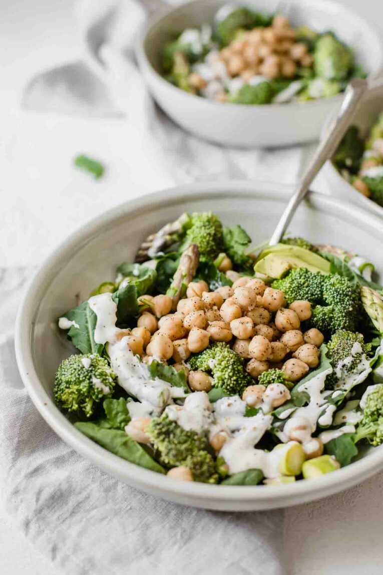Simple chickpea salad with broccoli, avocado, spinach, kale, asparagus, and yogurt dressing served in a grey bowl with a fork.