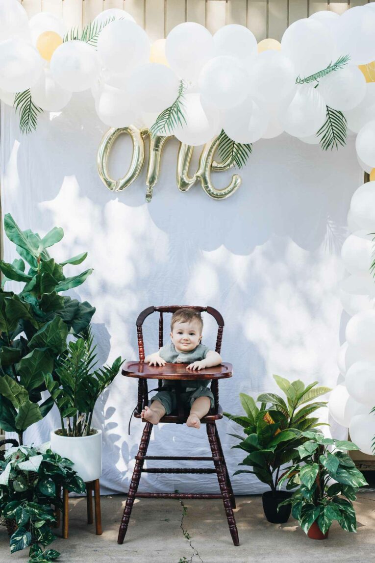 Tropical Plant First Birthday Party Tropical Plant First Birthday Party for baby boy. Boy sitting in high chair in front of 'one' backdrop.