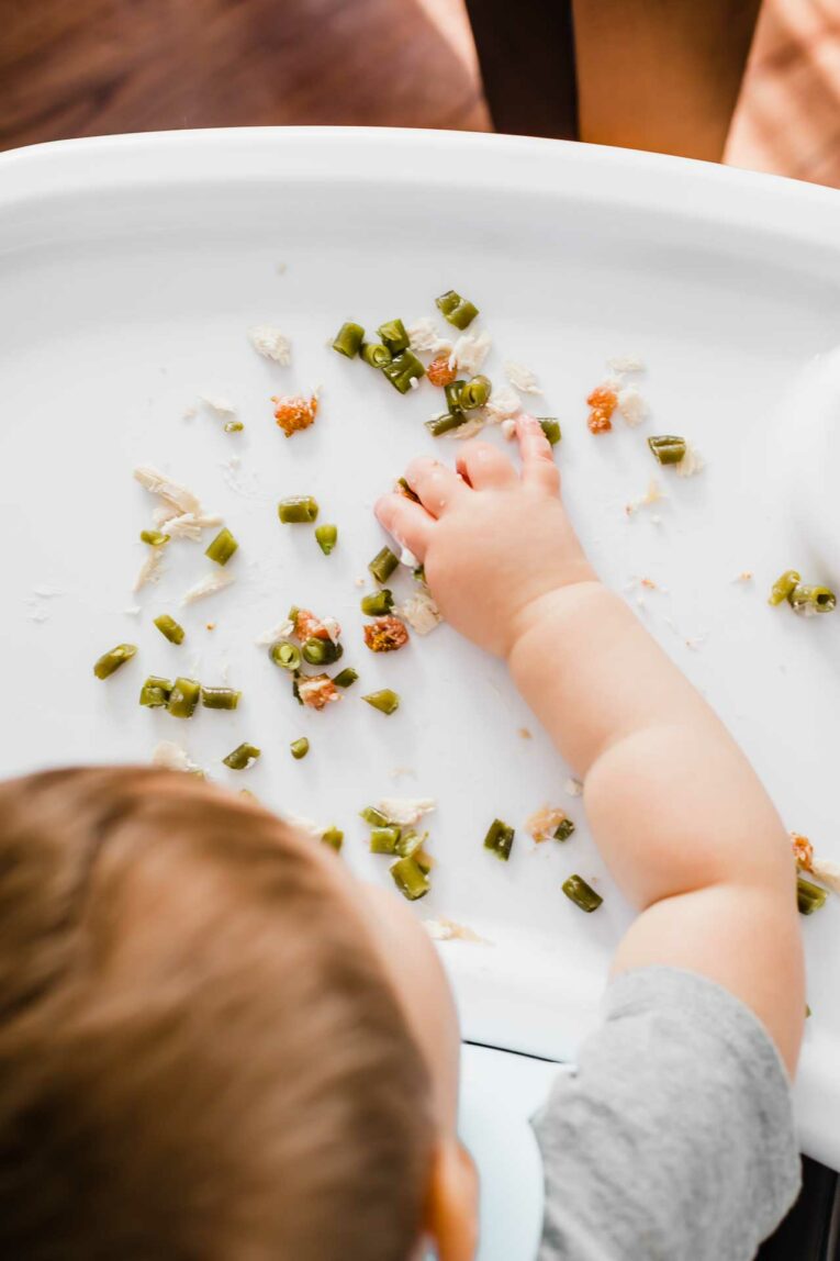 Want to get your baby started on finger foods? Here are 15 of the BEST, easiest, and simple baby led weaning recipes ideas! Baby eating solid foods on white high chair tray. (Baby led weaning recipes)