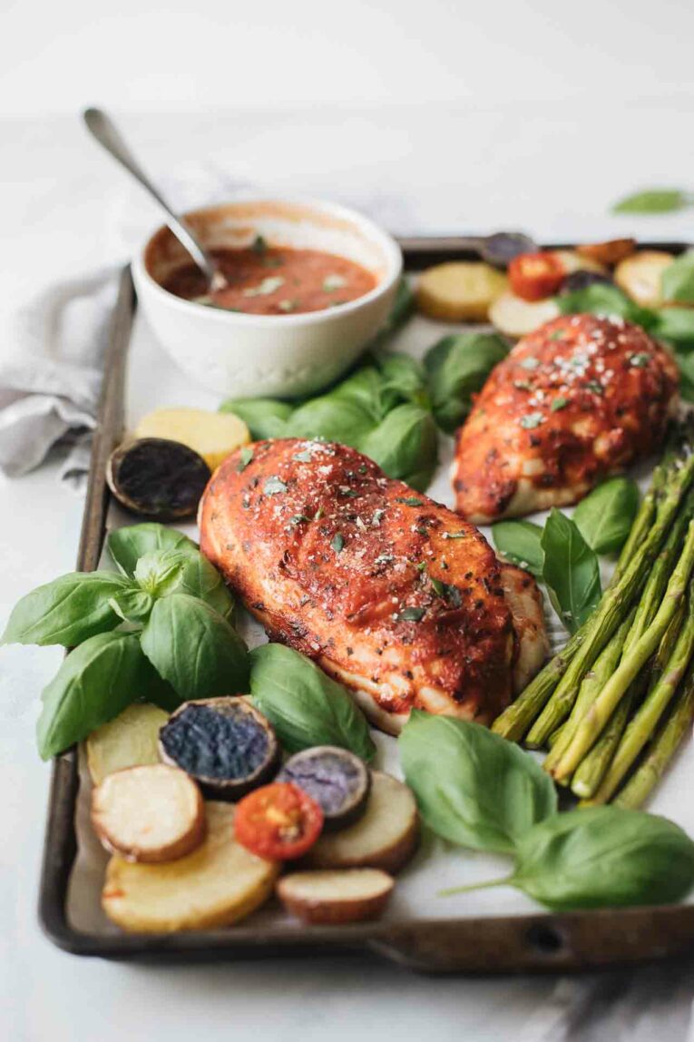Basil Chicken Sheet Pan Dinner that's savory and delicious. Made with organic chicken, roasted asparagus, baby potatoes, and topped with a tomato basil sauce that makes for the perfect, healthy, 30-minute dinner! Basil chicken on a sheet pan with baby potatoes and asparagus