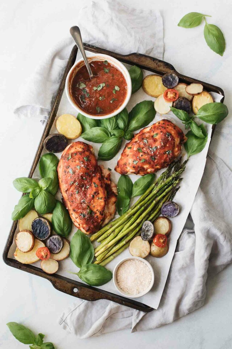 Chicken breasts baked with red sauce on a sheet pan with asparagus, potatoes, tomatoes, and basil.