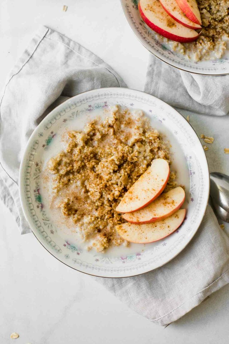 White Bowl full of Almond Milk, Cinnamon Quinoa Oatmeal, and Topped with Apples