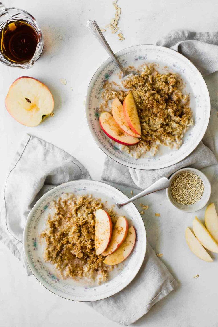 Sweet, wholesome, delicious, and easy to make. We're loving this simple Apple Cinnamon Quinoa Breakfast Bowl for a healthy start to the day! Apple cinnamon quinoa breakfast bowls on a table with apples and syrup.