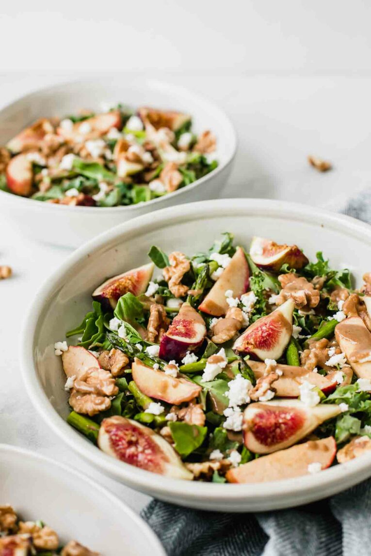 Goat Cheese Salad in a bowl topped with figs, walnuts, asparagus, apples, and a creamy balsamic dressing.