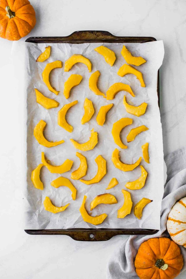 A sheet pan with white parchment paper and slices of roasted pumpkin.