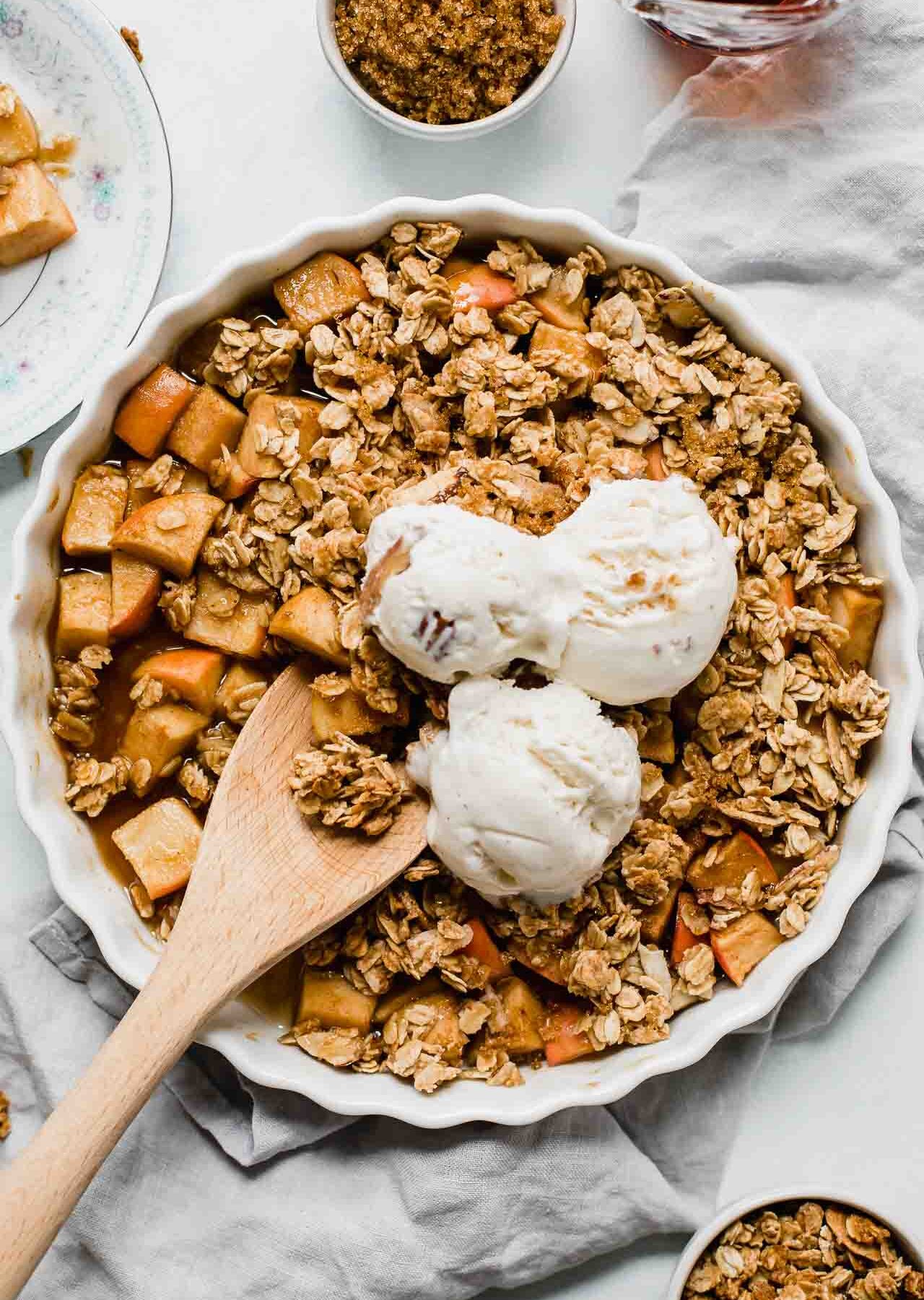 Healthy Apple Crisp in a tart dish with a wooden spoon.