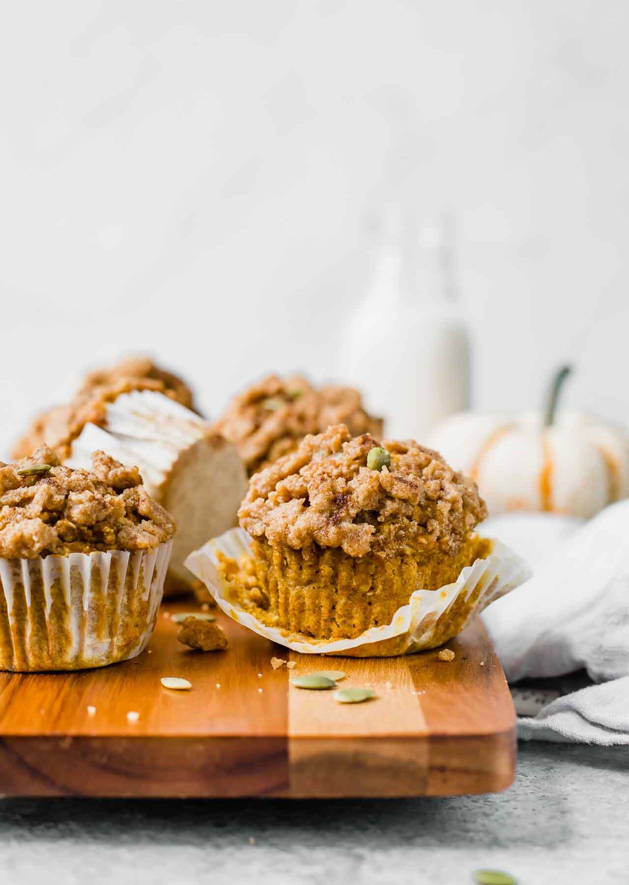 The BEST Healthy Pumpkin Muffins recipe on a cutting board with pumpkin in background.