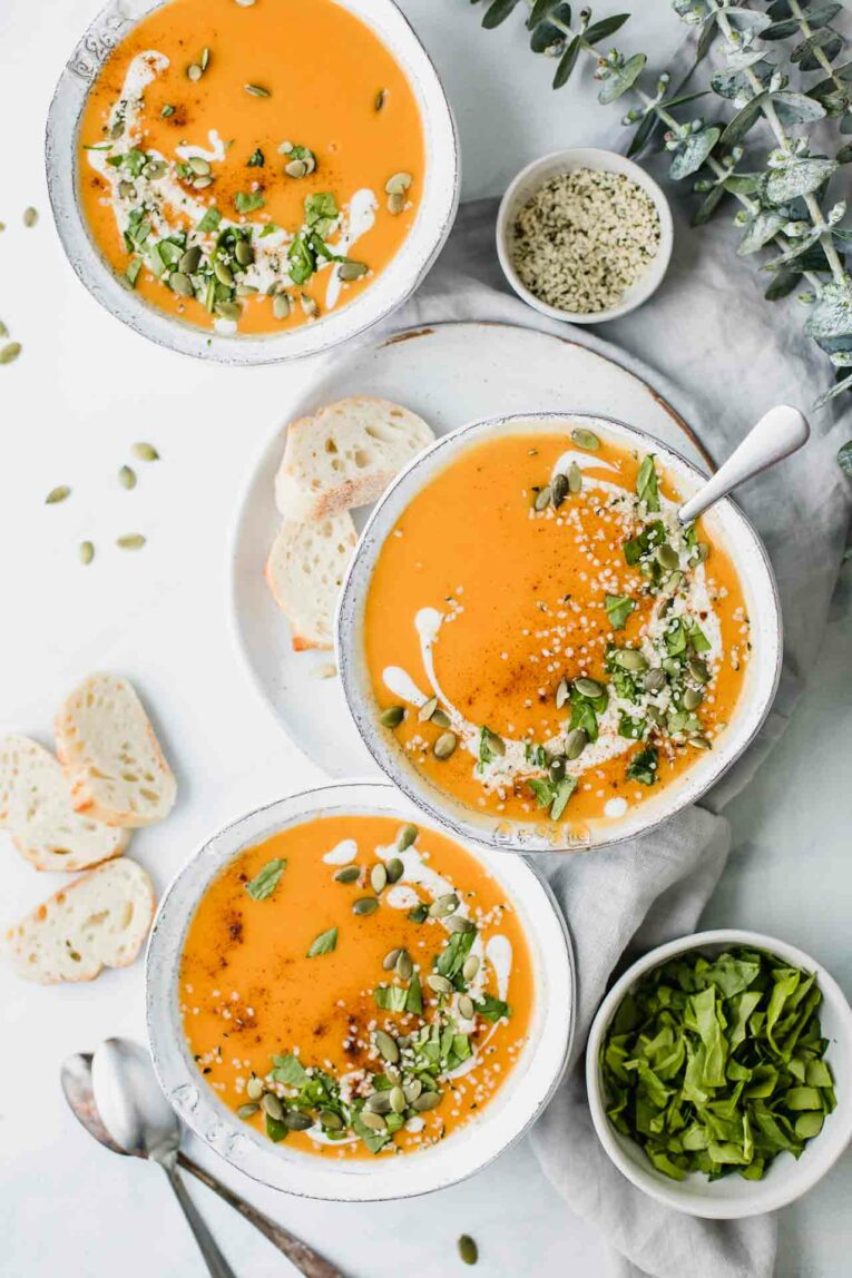 3 bowls of sweet potato soup served with baguette and spinach.