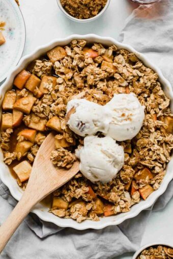 Healthy Apple Crisp in a tart dish with a wooden spoon.