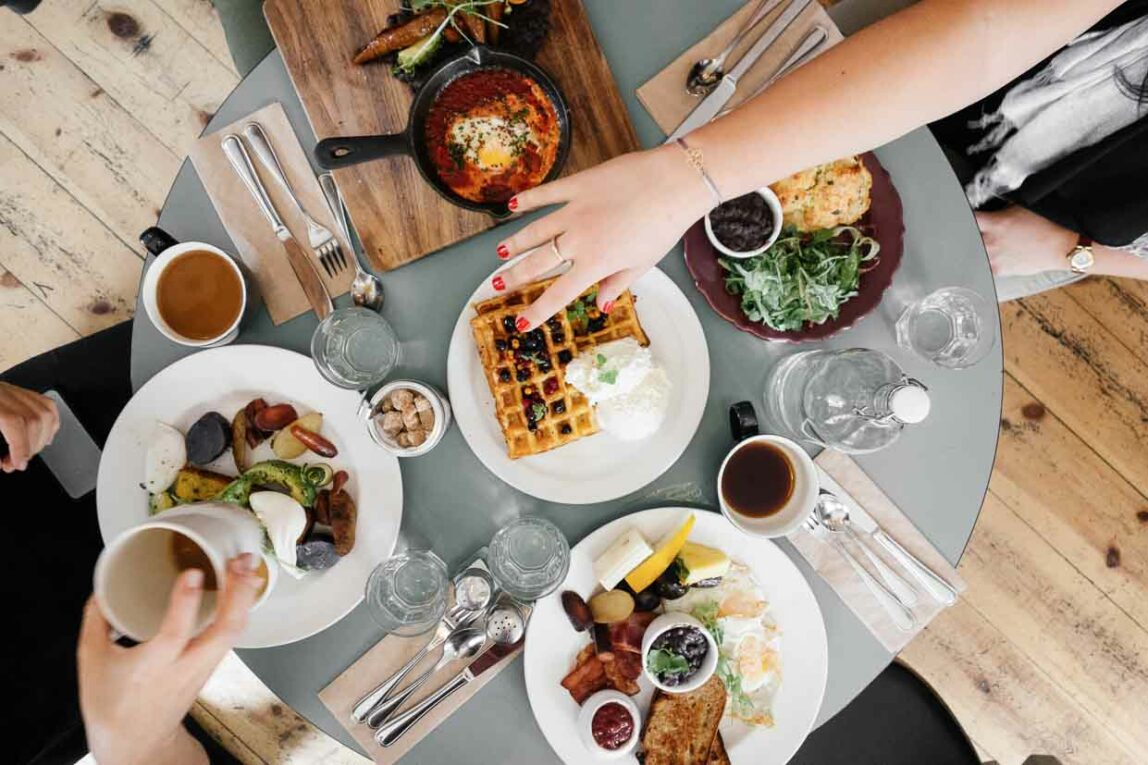 Brunch foods on a grey table with a hand reaching across.