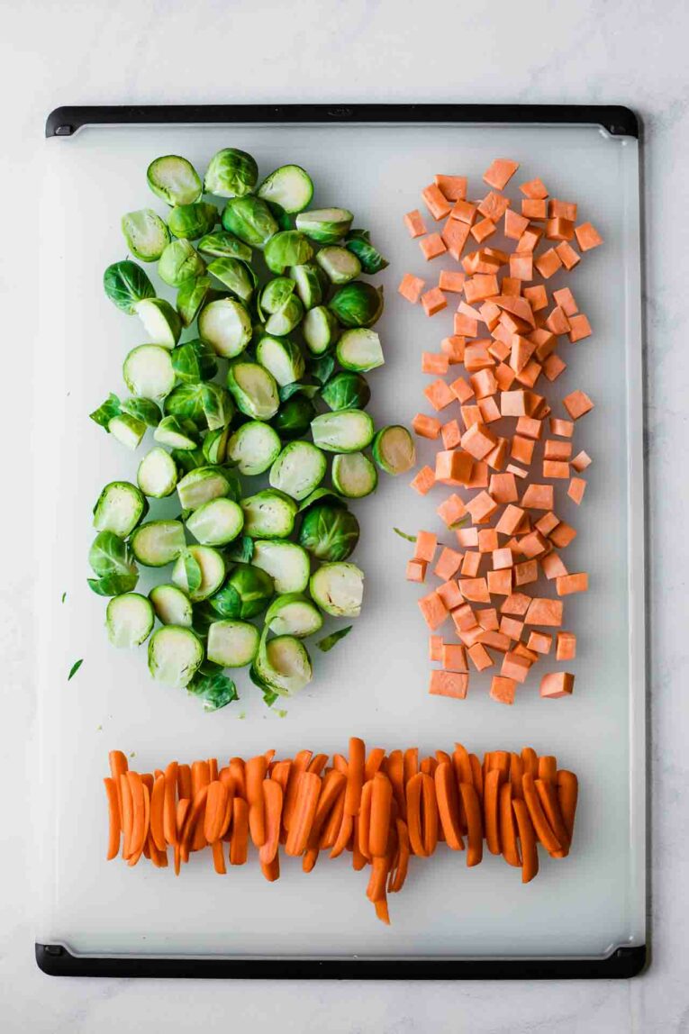 Brussels sprouts, sweet potatoes, and carrots on a baking sheet.
