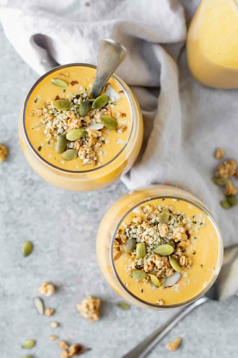 Top shot of two pumpkin smoothies with granola and seeds in glass cups.