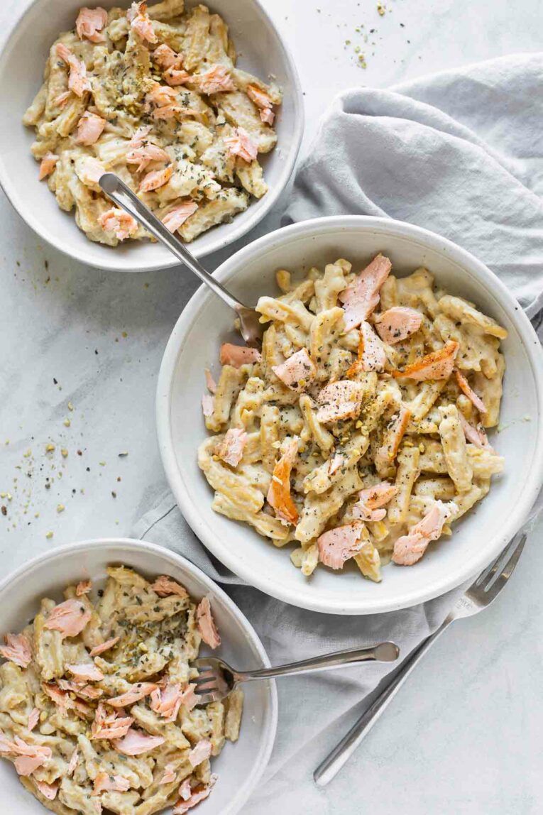 3 bowls of salmon pasta with a creamy sauce on a white background.
