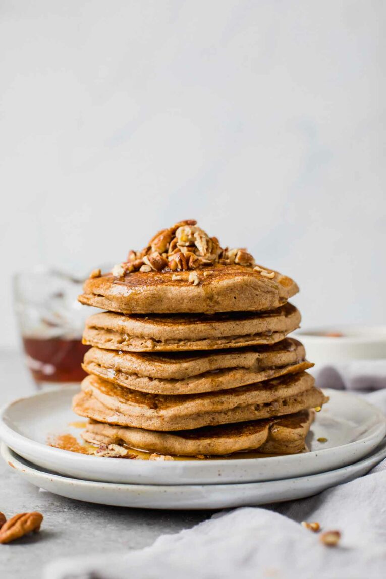 Fluffy pecan pancakes stacked with syrup and chopped pecans on a white plate.