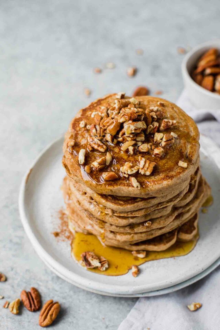 Angled shot of stacked pancakes with syrup and chopped pecans.