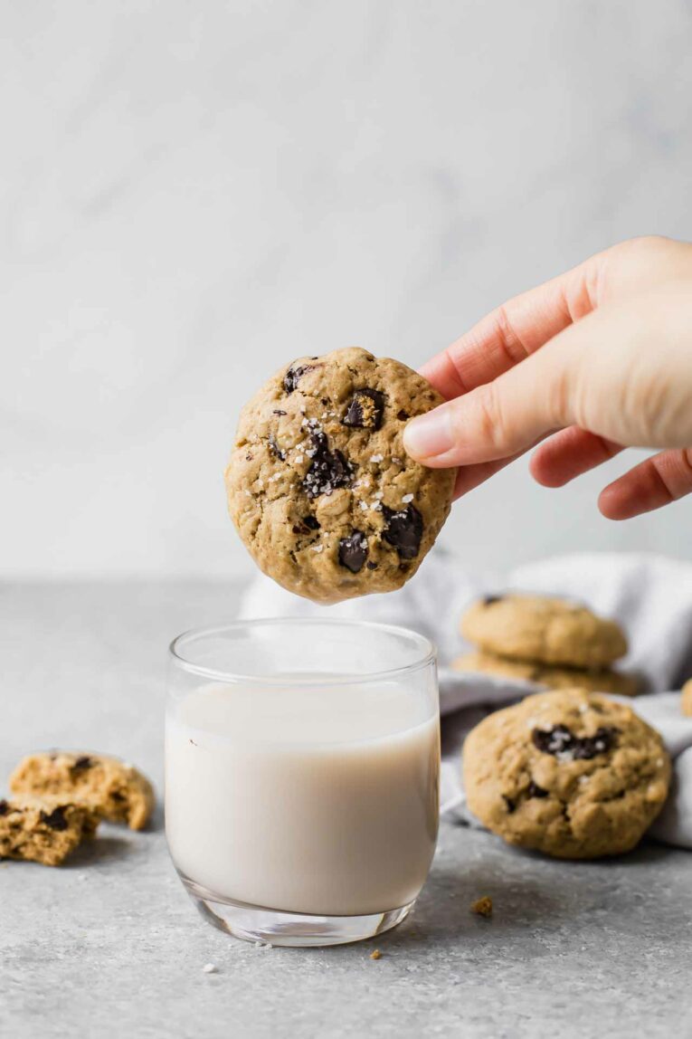 Hand dipping a Healthy Oatmeal Chocolate Chip Cookie in a glass of milk.