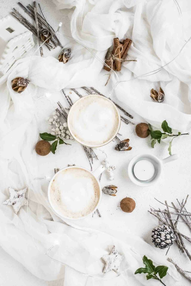 Two lattes on a white table with Christmas decor.