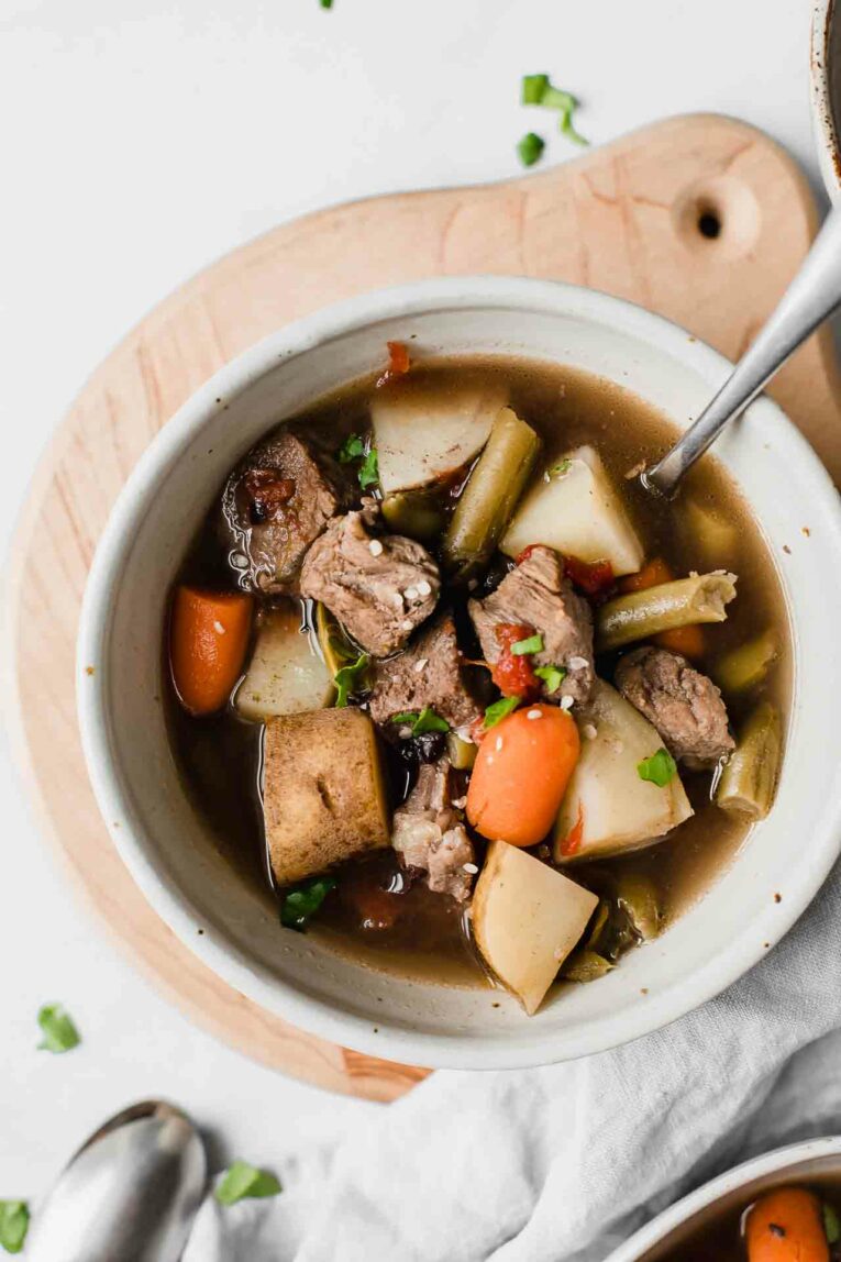 Close up of beef stew in a white bowl on a white table.