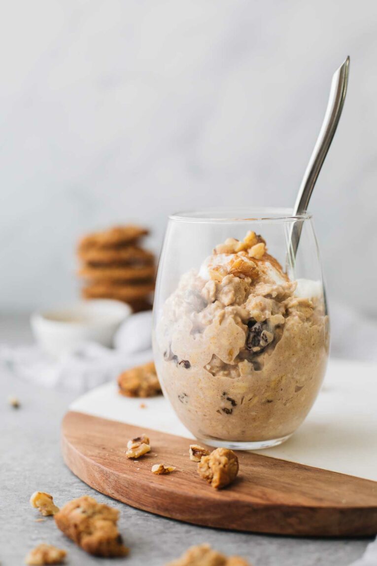 Glass of oatmeal cookie overnight oats with a spoon and cookies in the background.