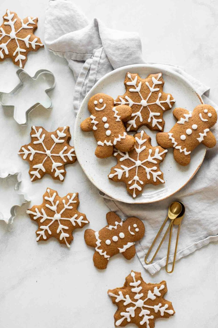 Gingerbread cookies spread across a marble countertop with cookie cutters and a plate.