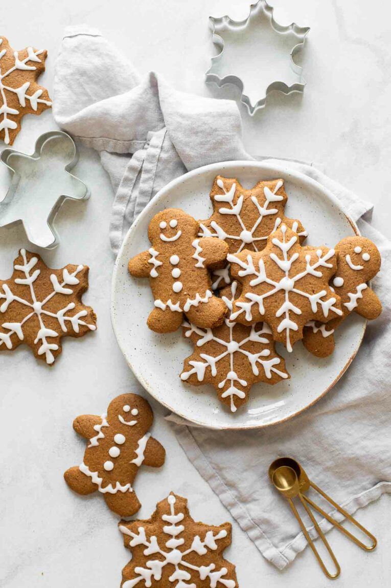 Gingerbread cookies on a white plate with cookie cutters and a napkin in the background.
