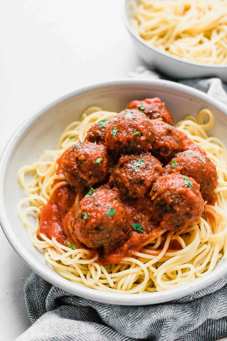 Angled shot of vegan meatballs in a red sauce over spaghetti in a bowl.