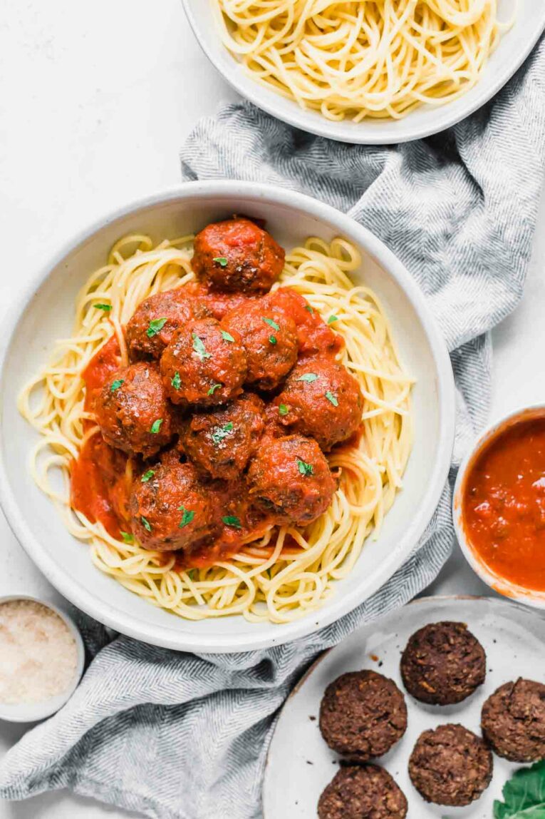 The BEST Easy Vegan Meatballs in a red sauce over spaghetti in a white bowl.