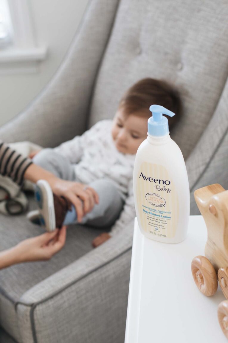 Aveeno Baby lotion in nursery with toddler putting on shoes in background.