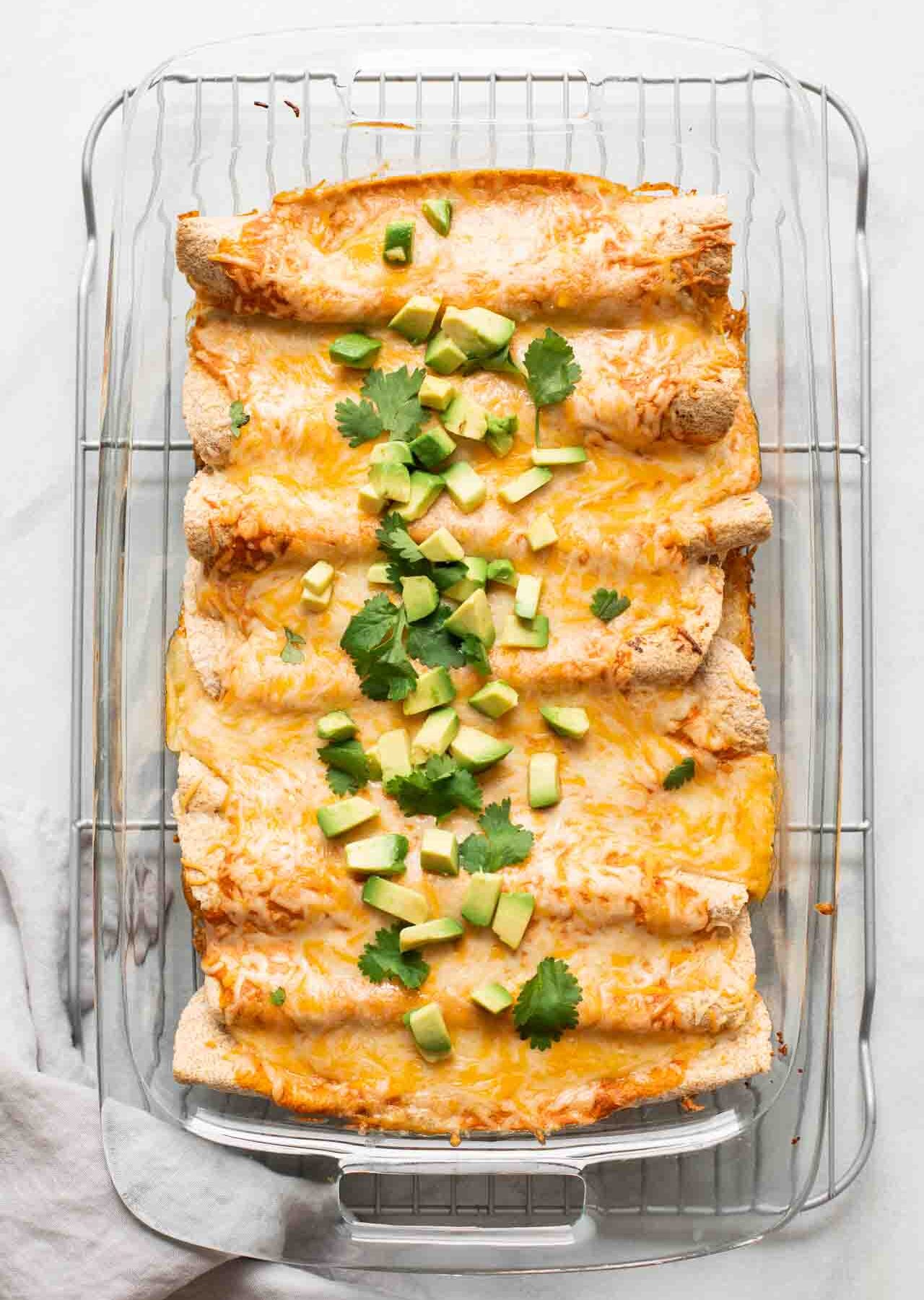 Top shot of enchiladas with shredded cheese, avocado, and cilantro.