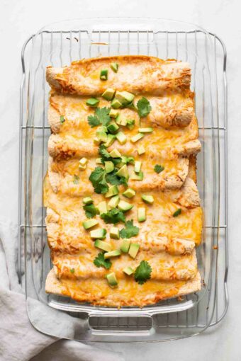 Top shot of enchiladas with shredded cheese, avocado, and cilantro.
