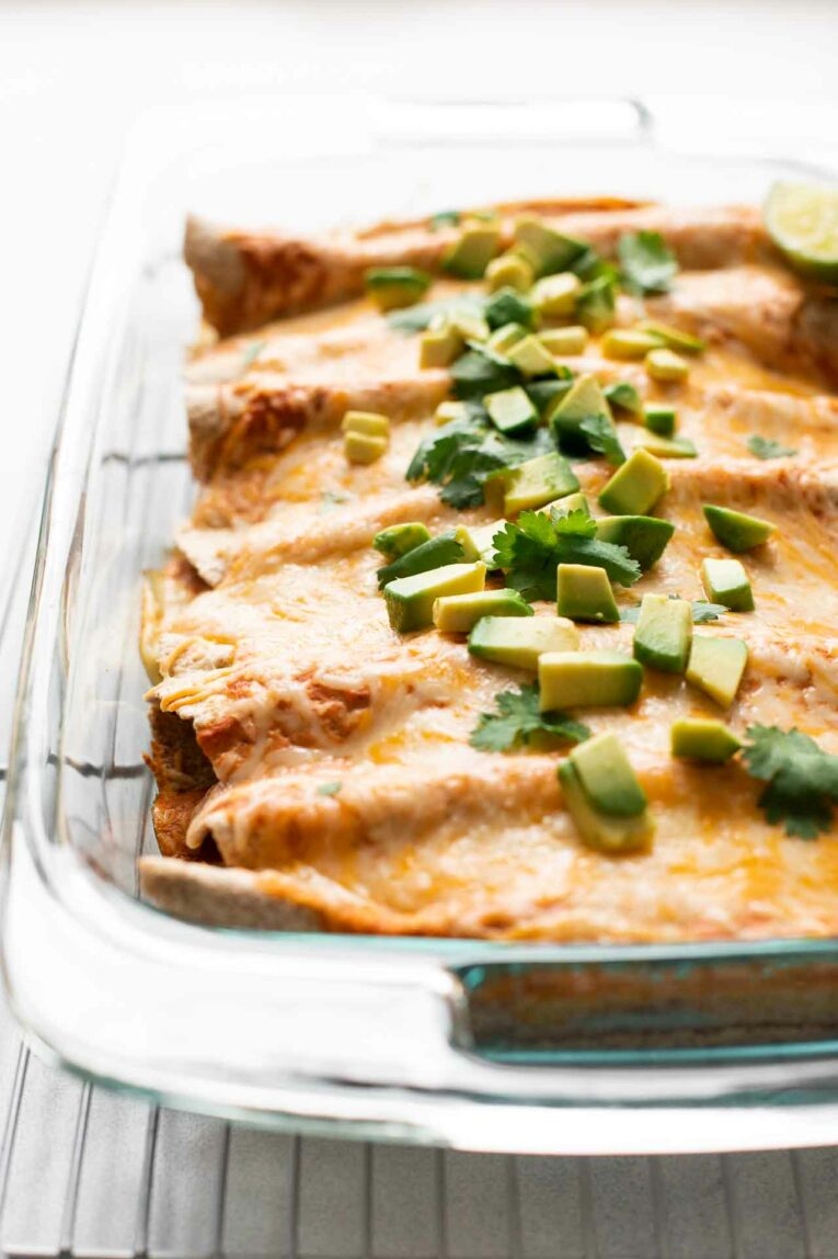 Top shot of enchiladas with shredded cheese, avocado, and cilantro.