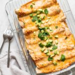 Vegetarian enchiladas in a glass casserole dish topped with avocado and cilantro.