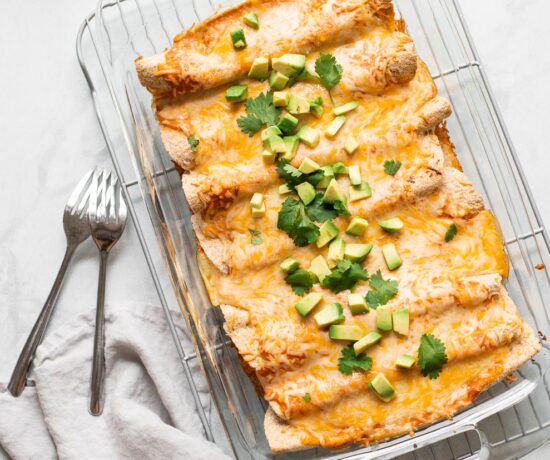 Vegetarian enchiladas in a glass casserole dish topped with avocado and cilantro.