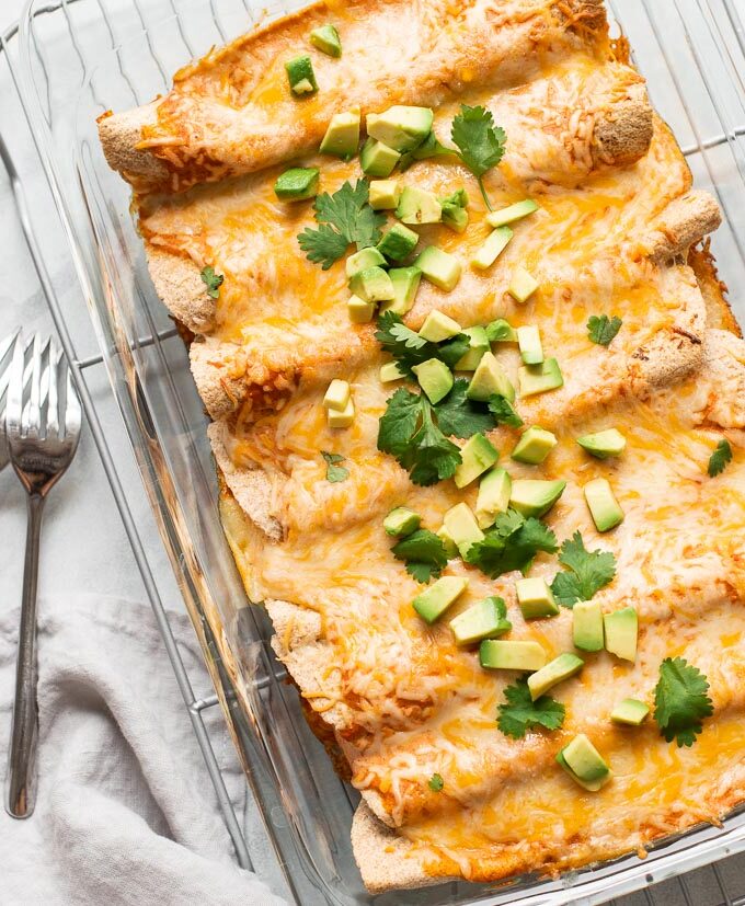 Vegetarian enchiladas in a glass casserole dish topped with avocado and cilantro.