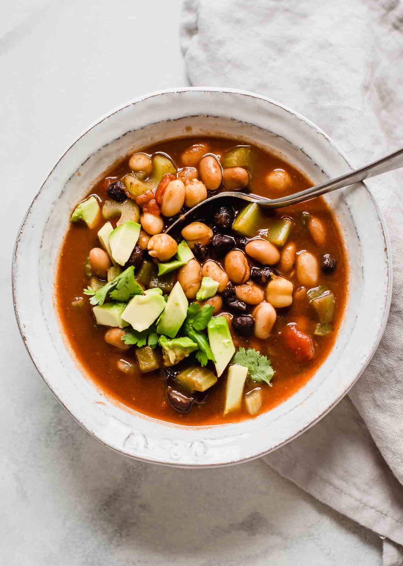 Top shot of vegan chili with avocado in a white bowl with a spoon.