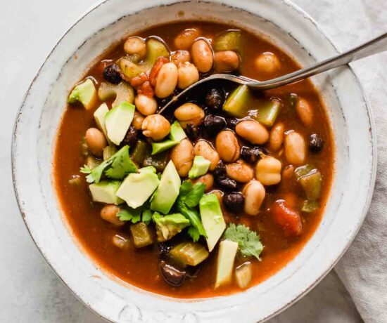 Top shot of vegan chili with avocado in a white bowl with a spoon.