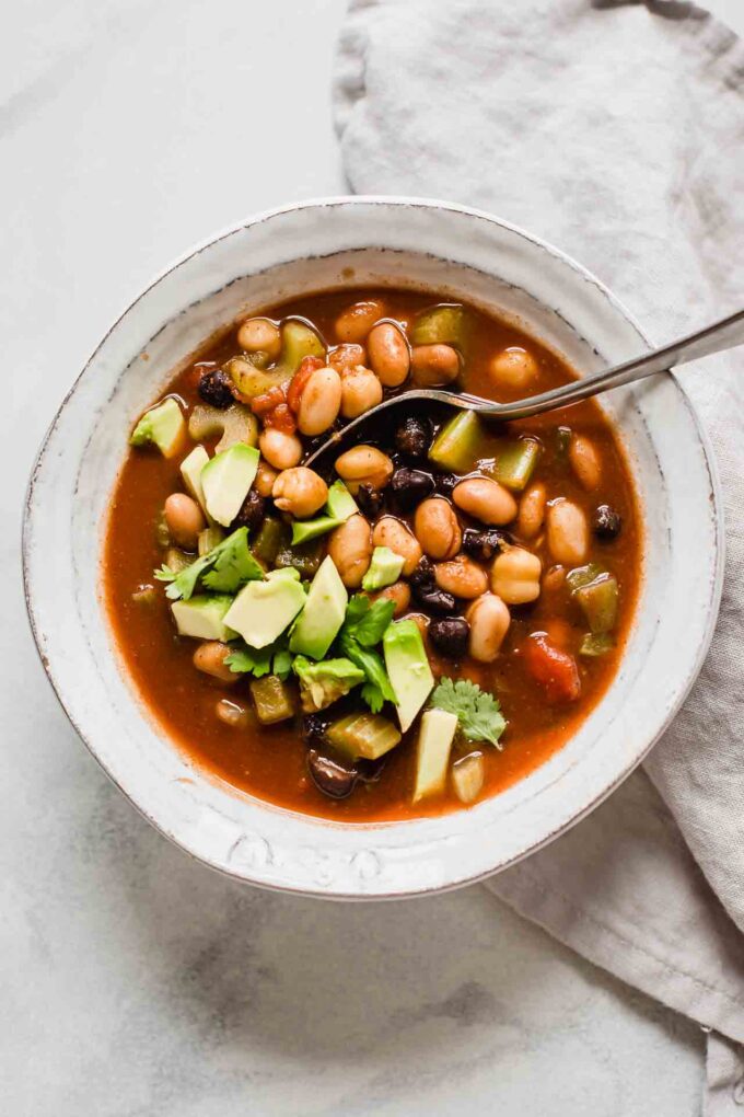 Top shot of vegan chili with avocado in a white bowl with a spoon.