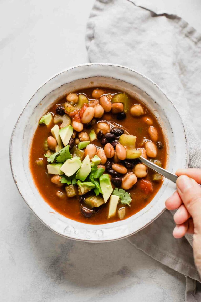 Vegan chili in a white bowl with a hand holding a spoon.