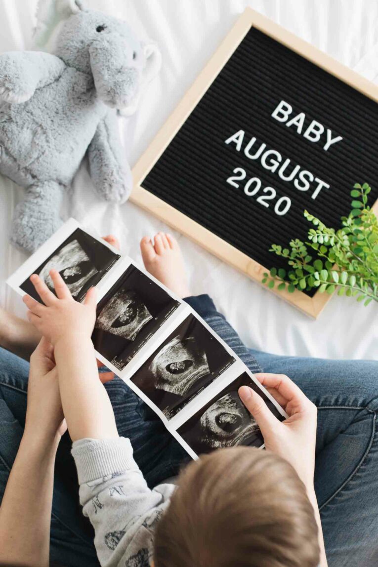 Top shot of mom and toddler holding sonogram for baby announcement.