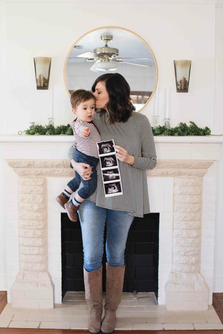 Mom kissing toddler and holding a sonogram for new baby announcement.