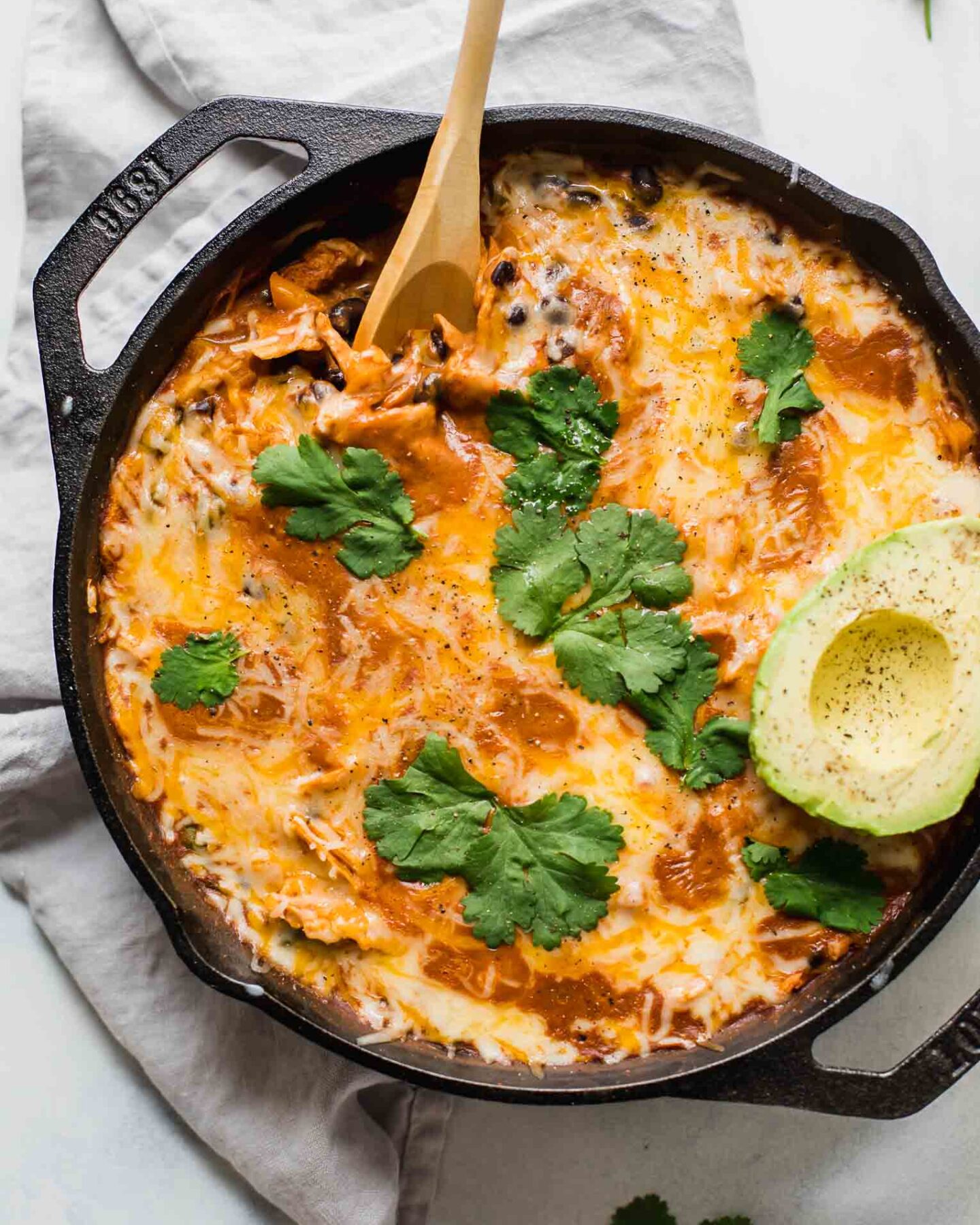 Top shot of Creamy Healthy Chicken Enchilada Skillet with a spoon and topped with cilantro and avocado.