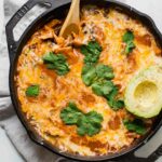 Top shot of Creamy Healthy Chicken Enchilada Skillet with a spoon and topped with cilantro and avocado.