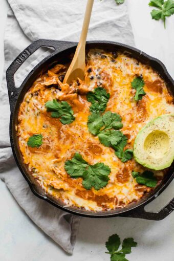 Top shot of Creamy Healthy Chicken Enchilada Skillet with a spoon and topped with cilantro and avocado.