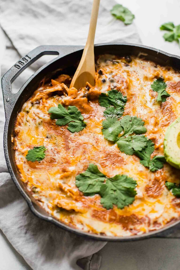 Side angle of creamy healthy chicken enchilada skillet on a grey napkin with a wooden spoon.