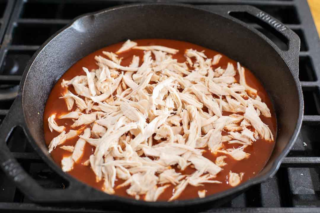 Shredded chicken in enchilada sauce in a skillet.