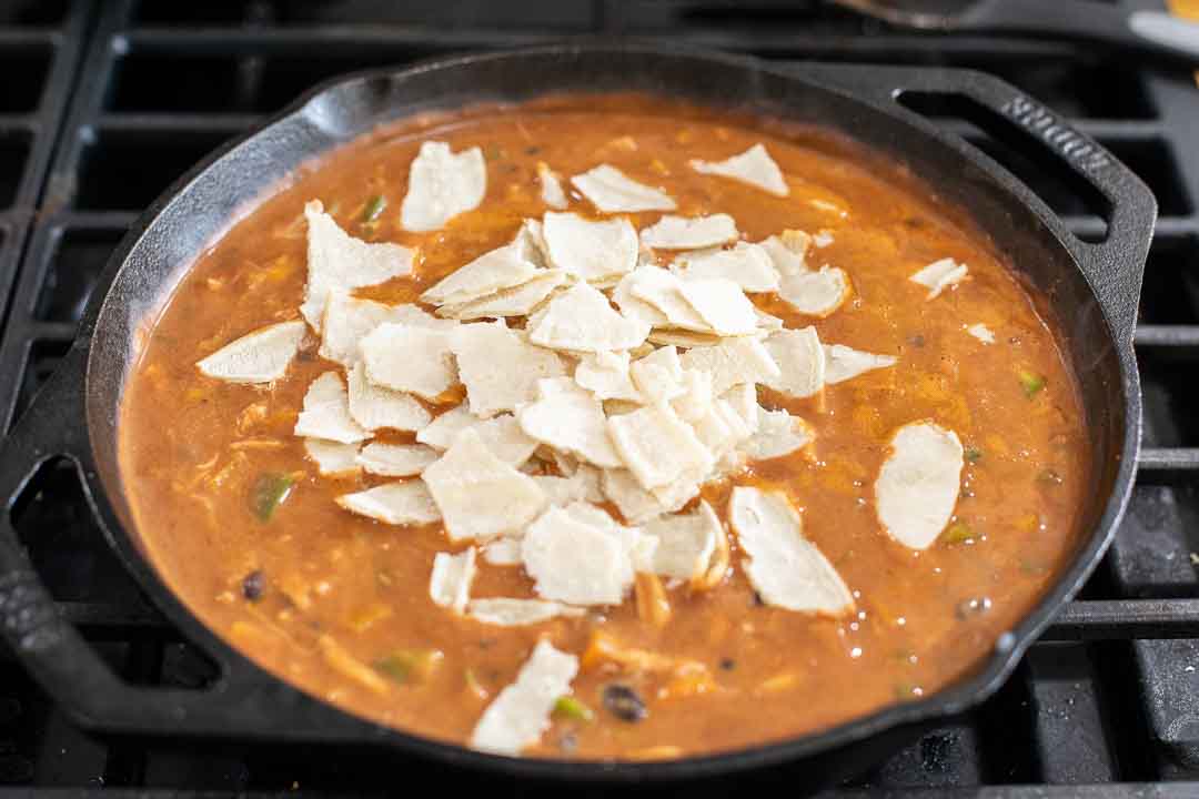 Corn tortillas cut into pieces and placed in a Chicken Enchilada skillet.