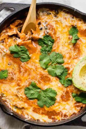 Top shot of Creamy Healthy Chicken Enchilada Skillet with a spoon and topped with cilantro and avocado.