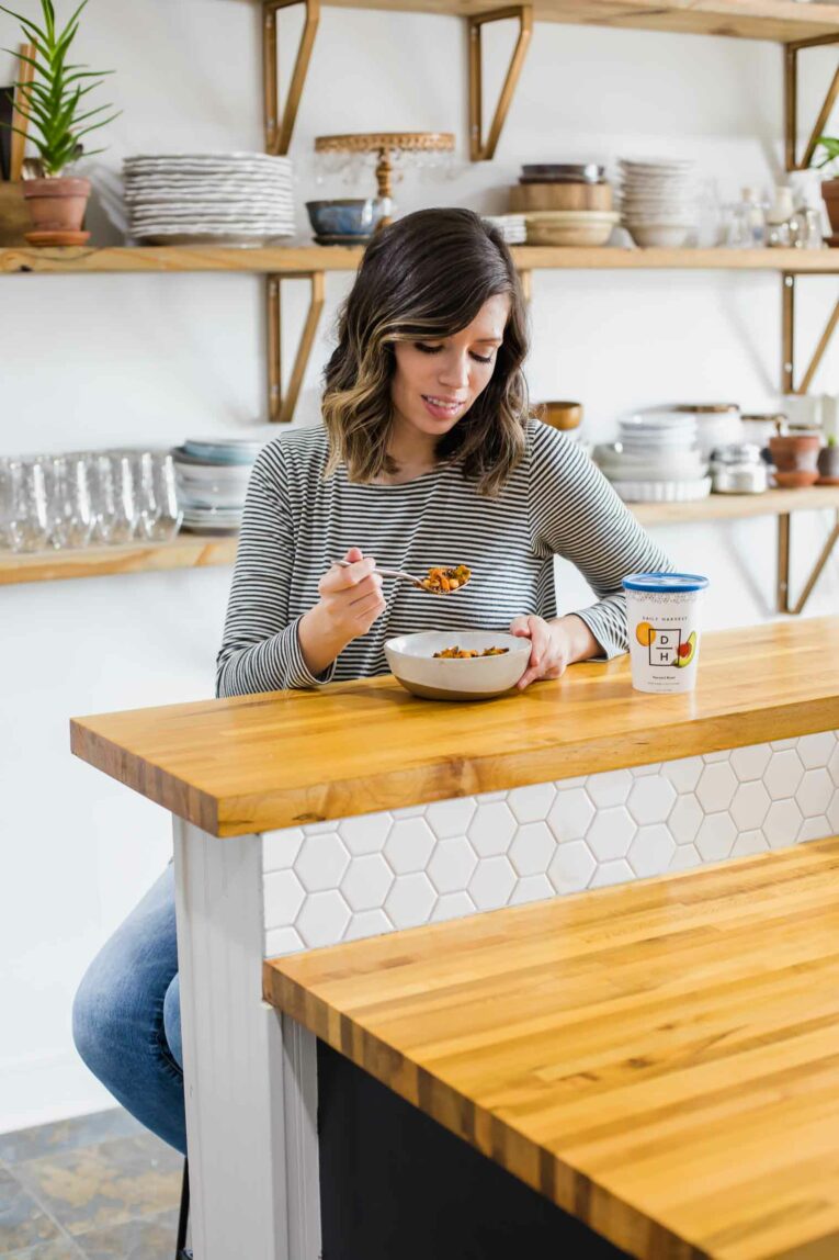 Woman eating harvest bowl in kitchen.